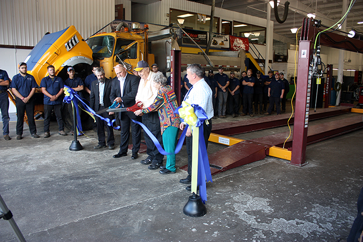 several people in front of a truck cutting a ribbon with scissors