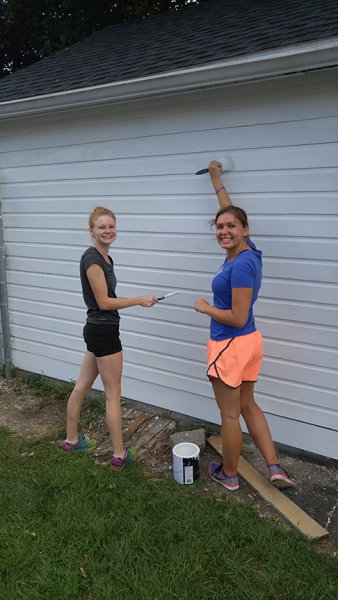 two girls painting the side of a white building