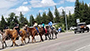 several people riding horses down a highway, cars behind them