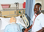 male student in nursing uniform standing next to a bed in a lab