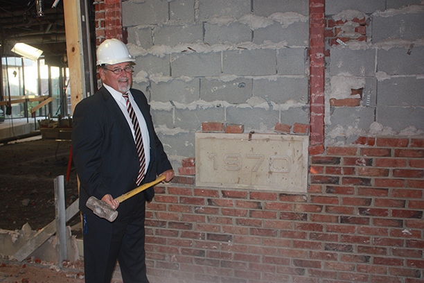 President Dr. Skip Sullivan at the MacKenzie Complex wearing a hard helmet and holding a hammer