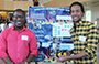 two male students holding their electrical engineering project, standing in front of a poster presentation