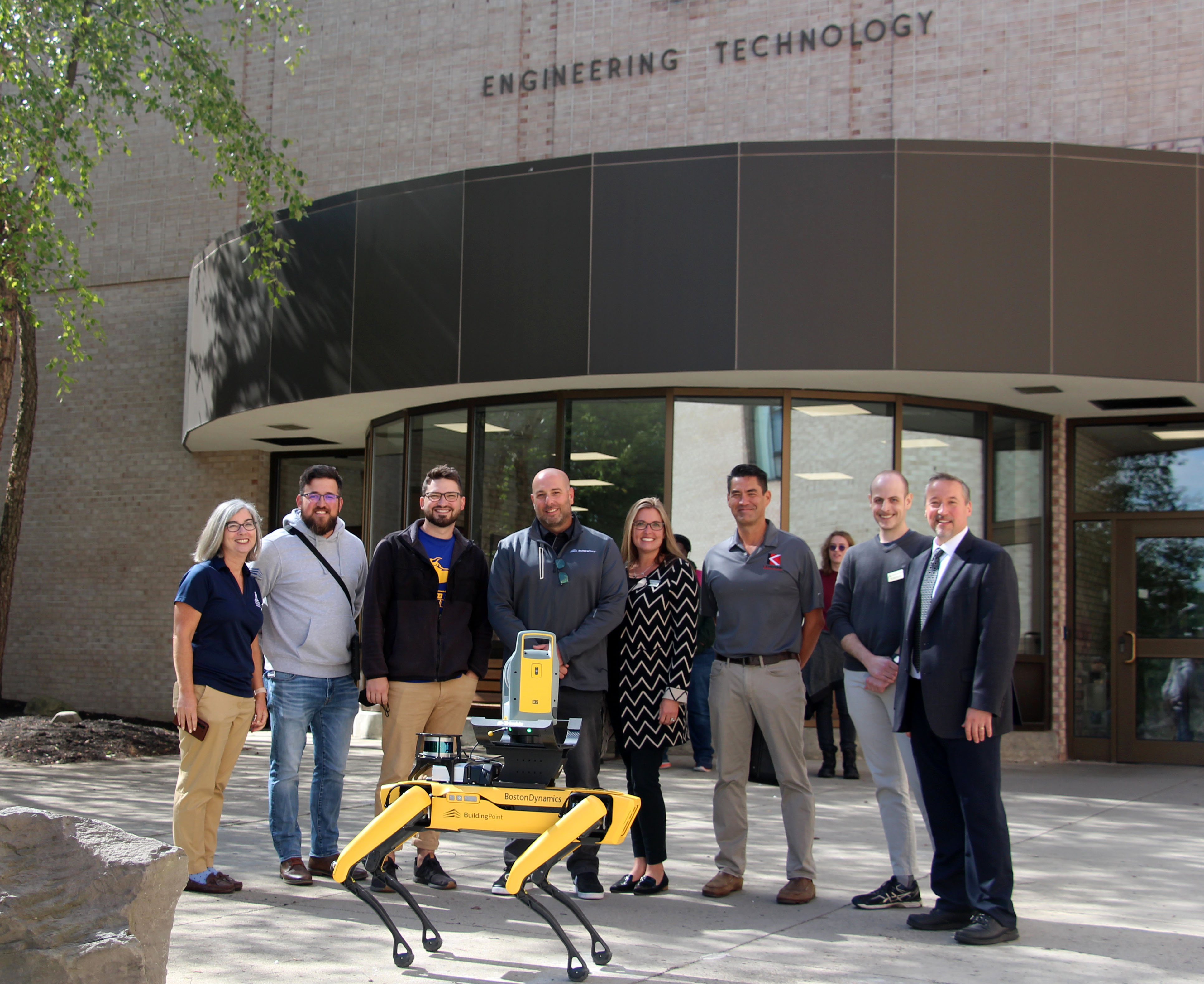 Group of individuals standing in front of building behind Spot the robot dog
