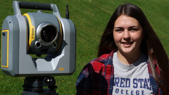 Students stands with surveying equipment