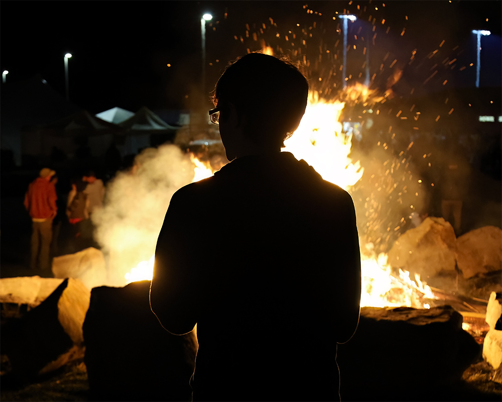 Photo of student standing in front of the bonfire in silhouette.