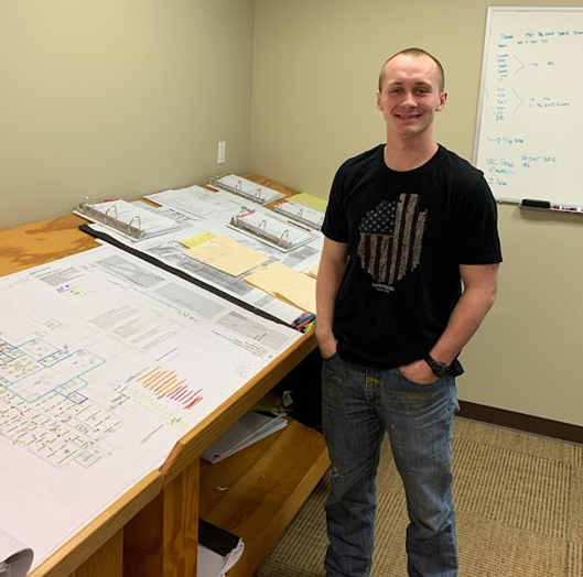 "student standing in front of a table with papers on it"