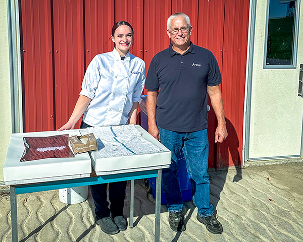 Photo of a culinary arts baking student standing next to Phil Schoeder at a food table at the farm.