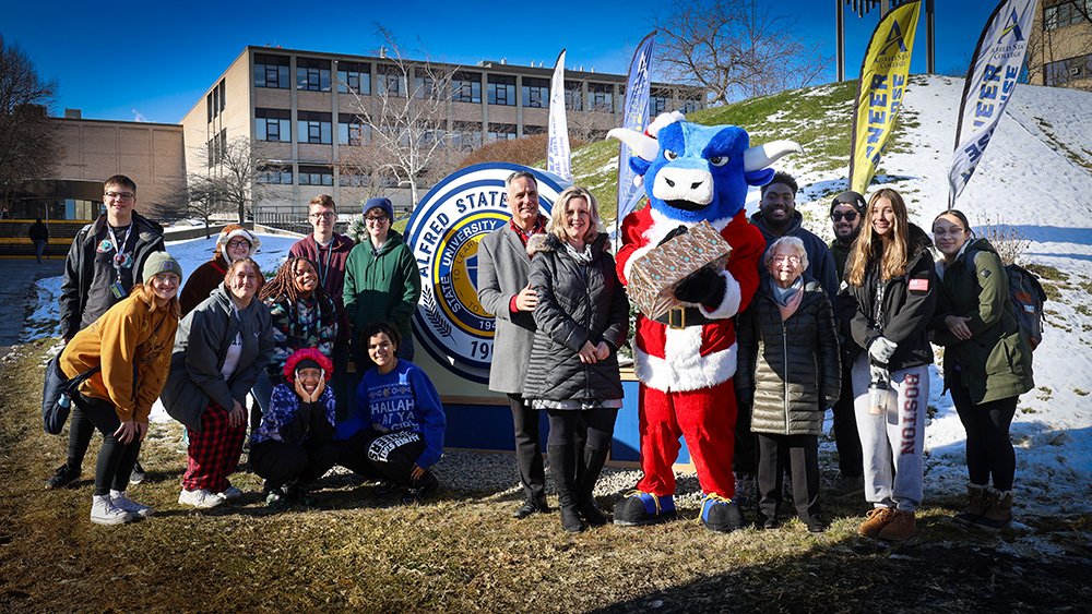Photo of the Mauros with students and Big Blue wishing you Happy Holidays from Alfred State.