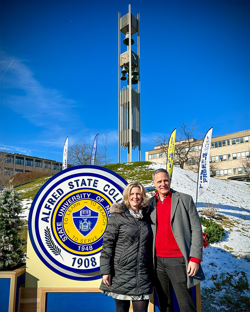 Photo of Melissa and Steve Mauro standing in front of the new college seal that sits in front of the Bell Tower.