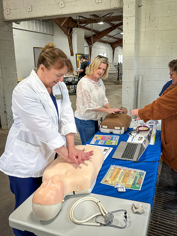 Photo of RuthAnne Ashworth teaching CPR techniques to Melissa Mauro with CPR manikins on a table.