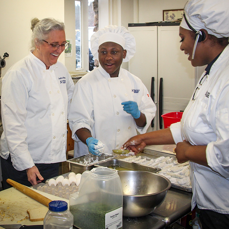 Photo of Deb Burch with ASC culinary students preparing food.