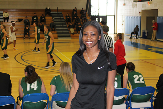 female in gymnasium with basketball game in background