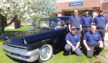 five students standing in front of a car