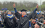 student at commencement pointing to the sky
