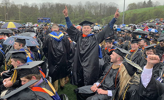 student at commencement pointing to the sky