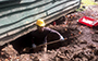 student wearing hard hat digging a hole underneath the house