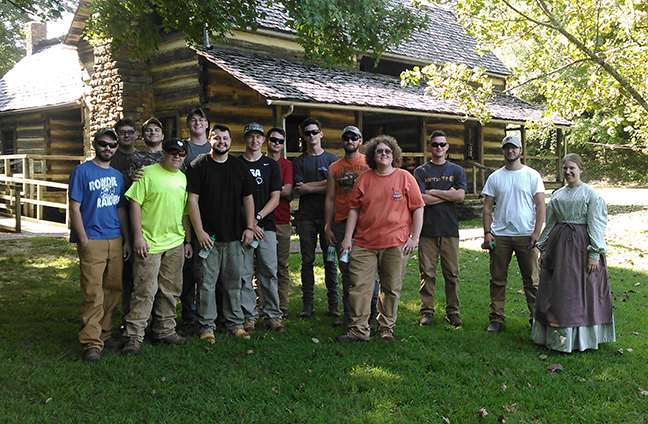 students standing outside a log cabin