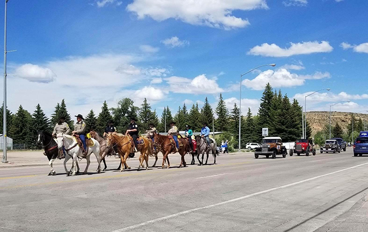 several people riding horses down a highway, cars behind them