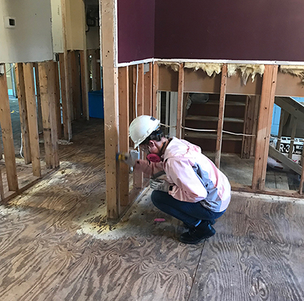 student wearing a white hard helmet prepares studs for mold sanitation