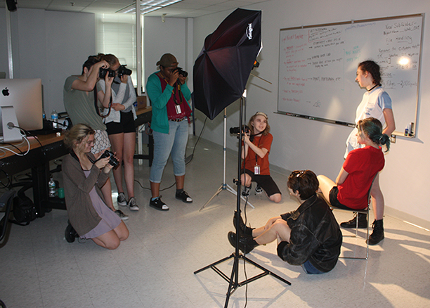 students in the photography class of the NYSSSA School of Media Arts, holding cameras and a light shining on students