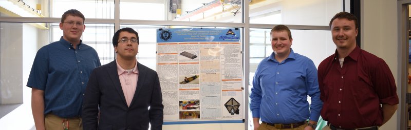 four male students standing next to a poster board