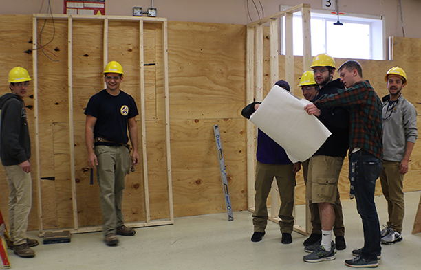 students looking at floor plans, wearing yellow hard helmets