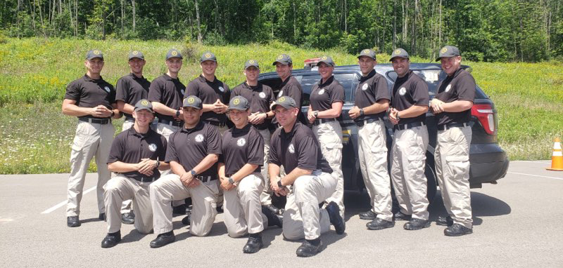 academy recruits in uniform standing in front of a vehicle