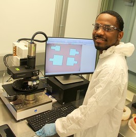 student wearing a white suite standing in front of a computer