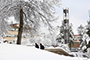 snow, trees, and bell tower on campus, two students