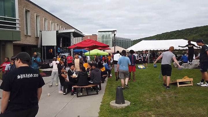 students playing games outside on lawn, umbrellas and tables in front of SLC building