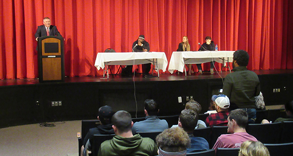 man at podium and students sitting at tables on stage