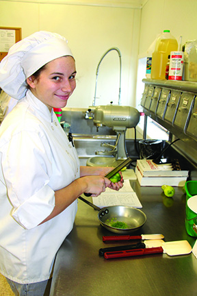 female culinary student in uniform holding a large pot