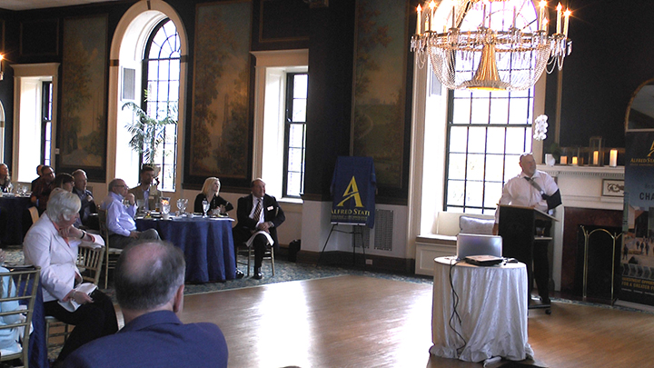 several people seated at tables inside a restaurant with a speaker at front of the room