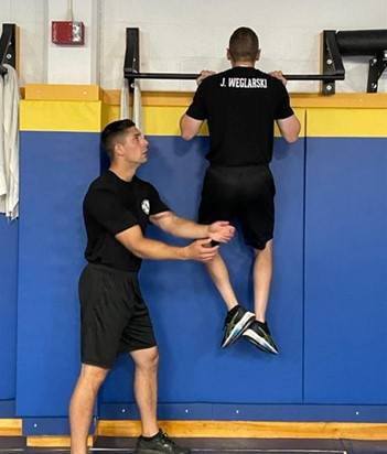 two students one is doing a chin up while the other is spotting