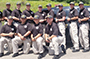 recruits standing in front of a vehicle, all wearing tan pants and a black shirt