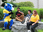 mascot Big Blue sitting on a stone with students on campus