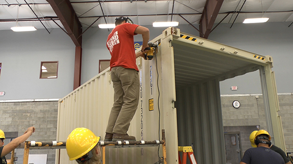 students wearing hard helmets using tools on a shipping container