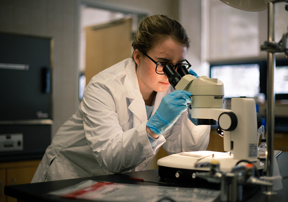 Forensic science student making observations through a microscope.