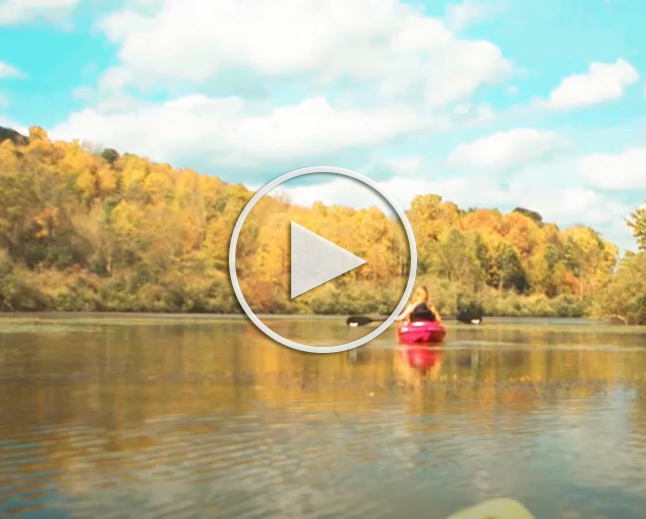 canoe on a river with trees and changing leaves, play button to youtube video