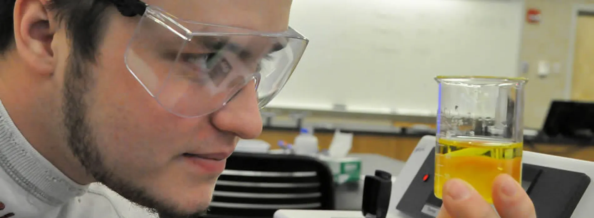 male student looking into a beaker with yellow liquic