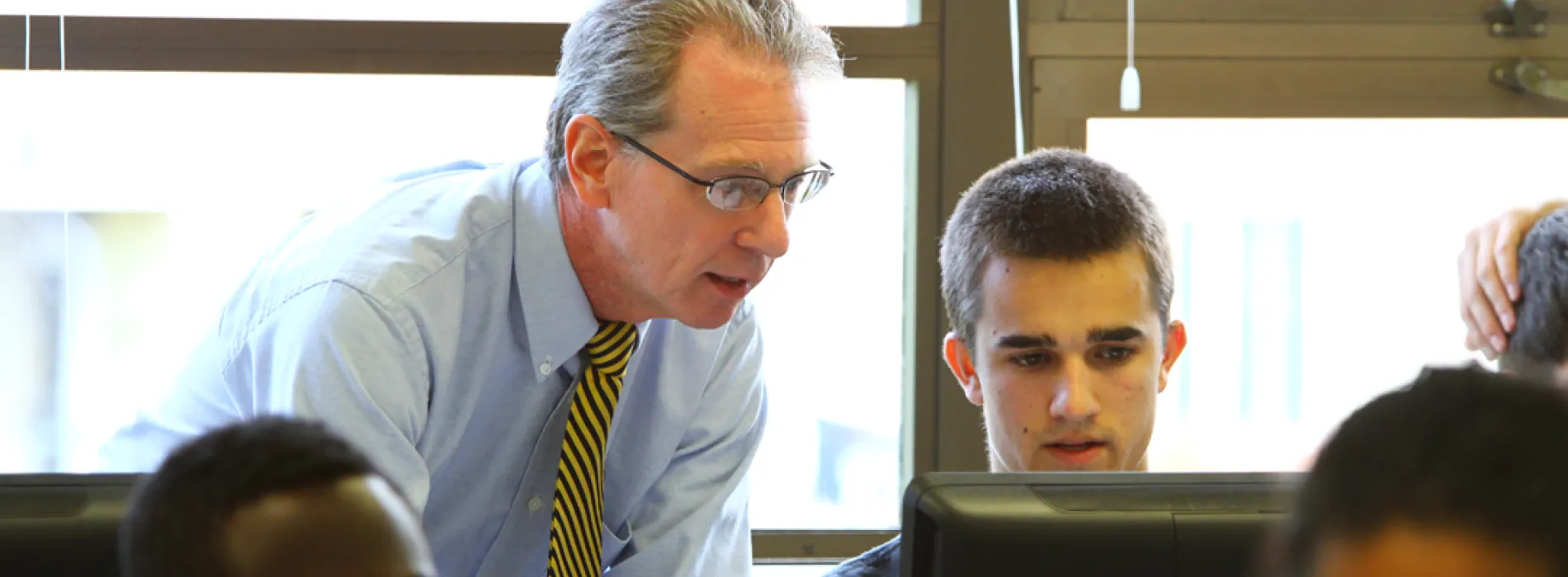 male professor looking over the shoulder of male student at a computer
