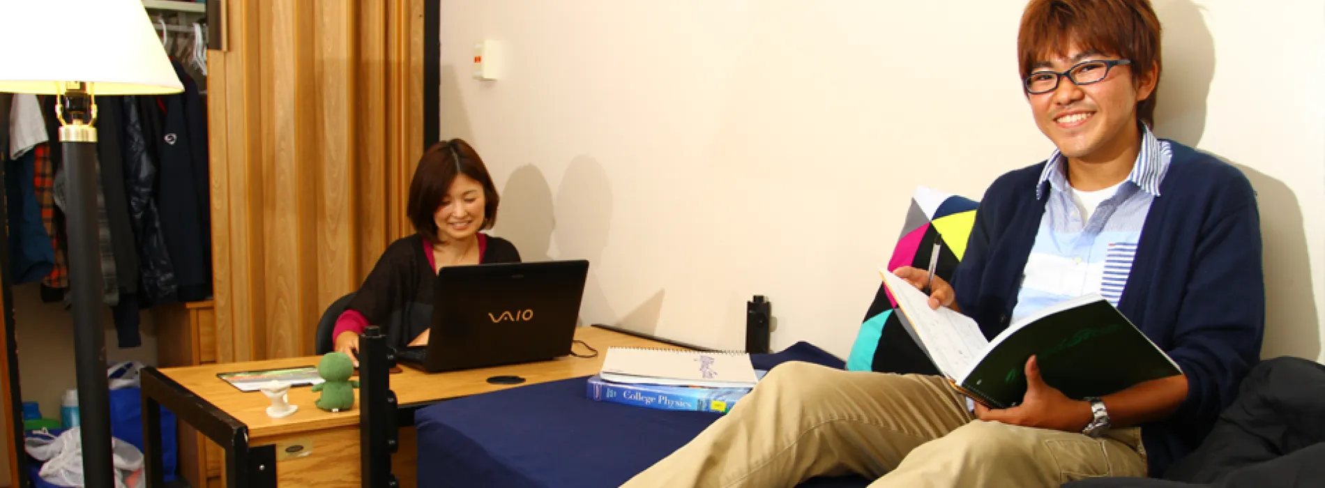 female student sitting at a desk and male student sitting on a bed in residence hall