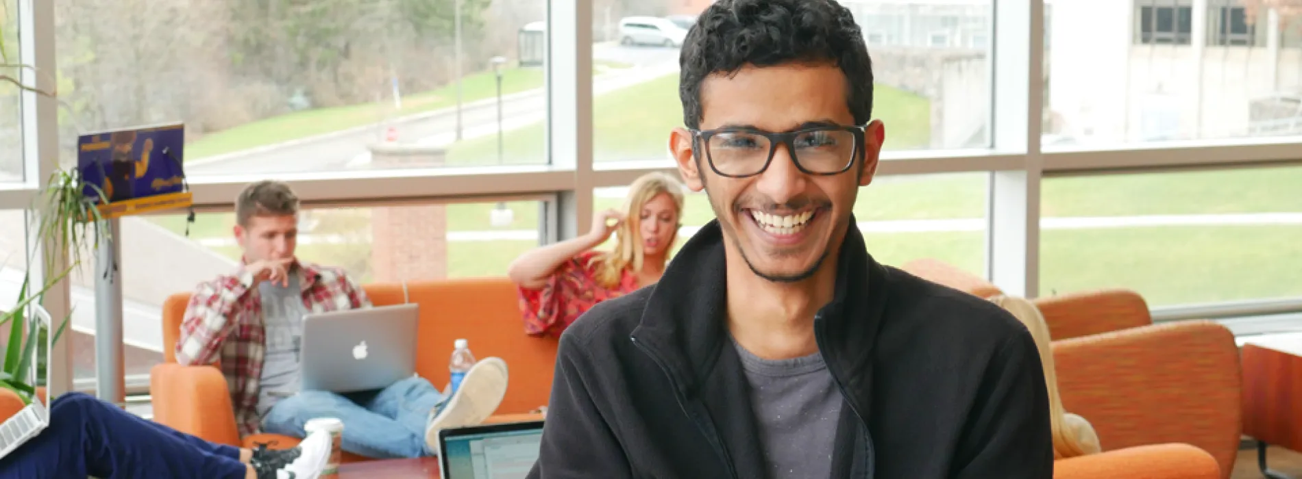 Male international student laughing as friends study behind him at Student Leadership Center