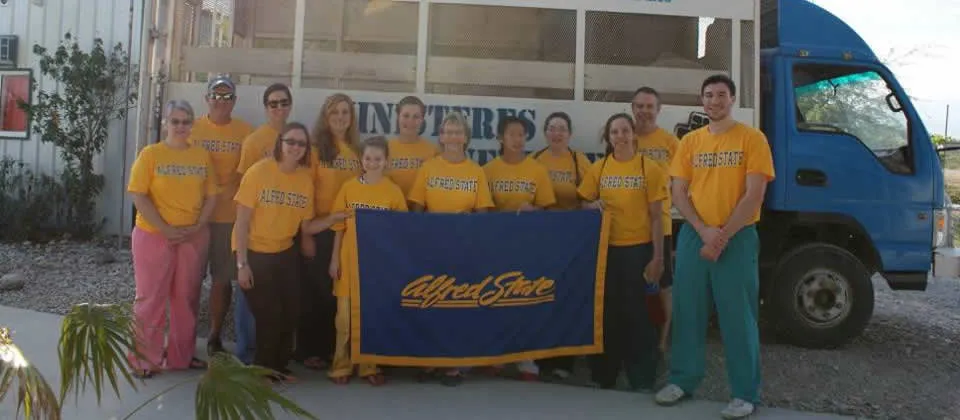 several people wearing yellow shirts that say Alfred State, holding a blue Alfred State banner