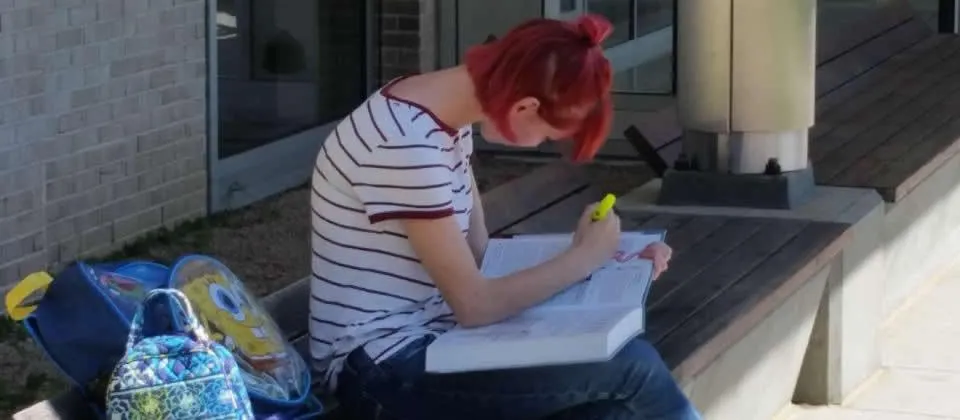 female student reading book sitting on a bench