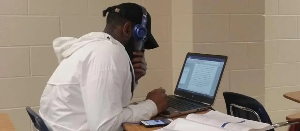 student wearing a hat sitting at a table with laptop