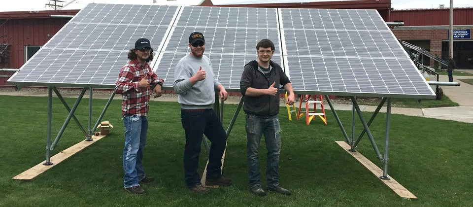 three male students in front of a solar panel on campus