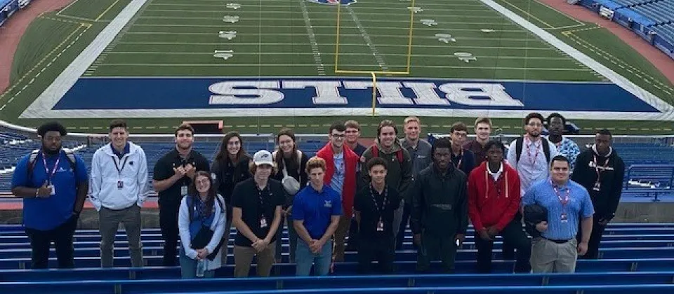 students standing in bleachers of Highmark Stadium in front of Buffalo Bills field
