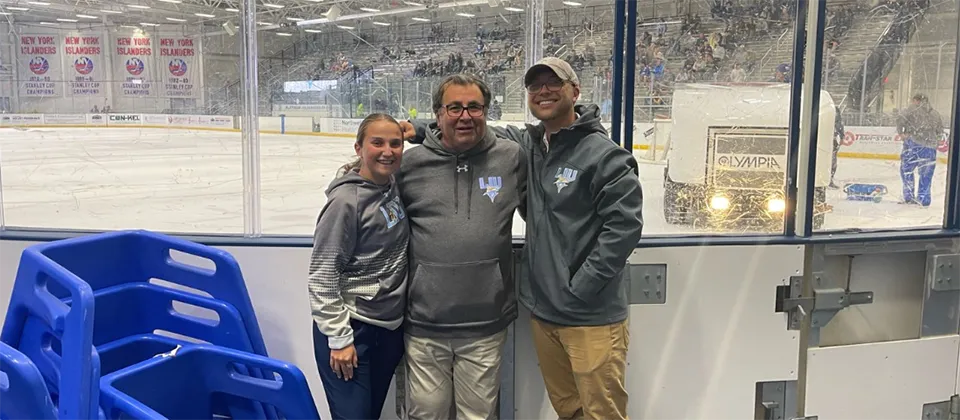 three people standing in front of a hockey rink glass wall