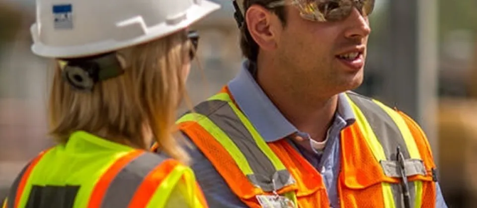 female and male wearing vest, safety glasses, and hard hat